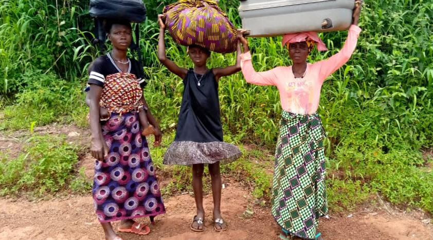 3 women hold their belonging in bags on their heads